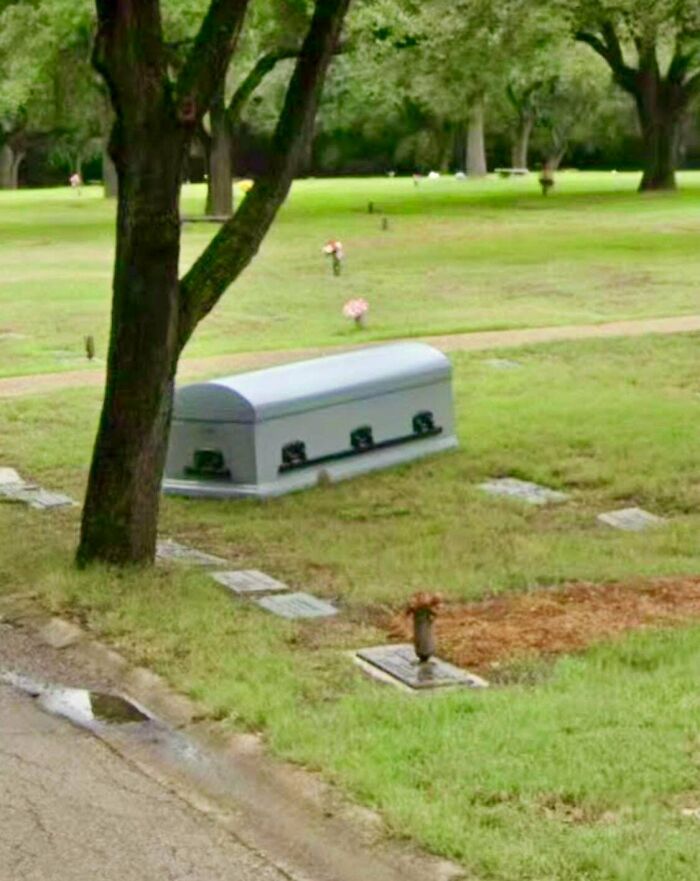 Coffin lowered underground in cemetery with strange visible casket top
