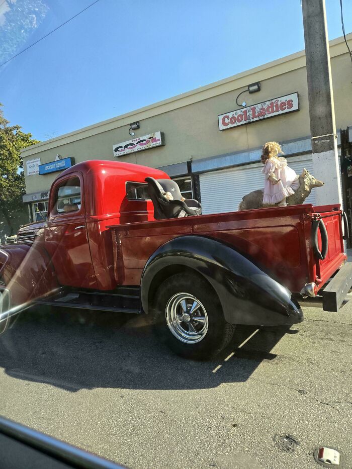 Vintage red pickup with car seat and doll in trunk parked outside Cool Ladies store