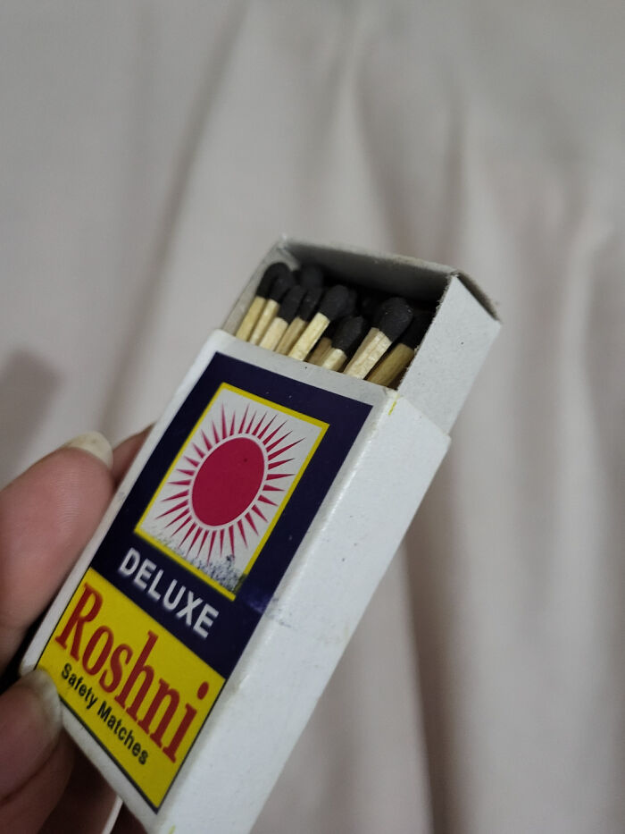 Open box of Roshi safety matches with black match heads in hand