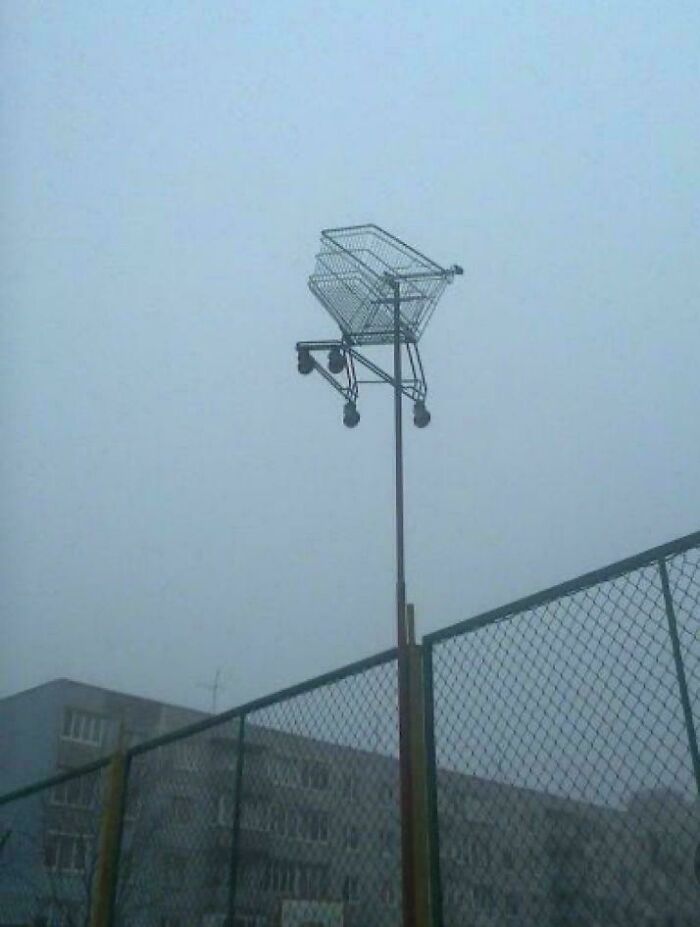 Shopping cart mounted high on a tall metal pole above a fence in foggy weather