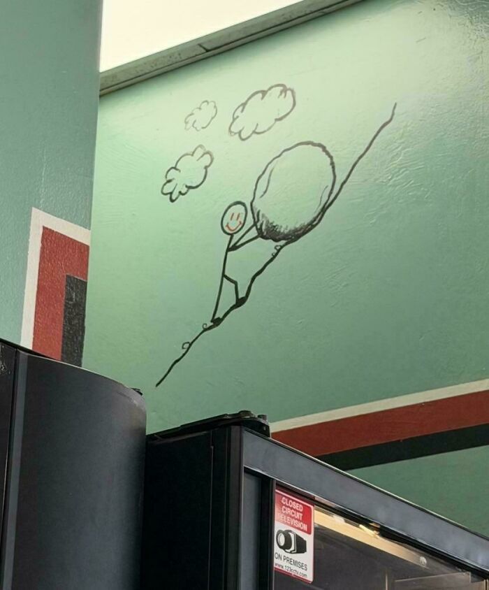 Wall mural of a stick figure pushing a large rock uphill with clouds above