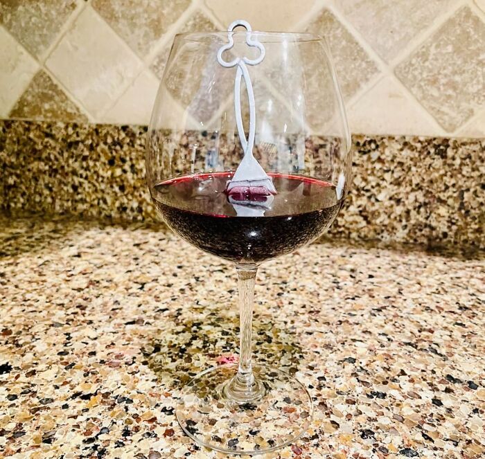 A wine glass with red wine and a teabag-shaped wine marker, a humorous Mother's Day gift idea.