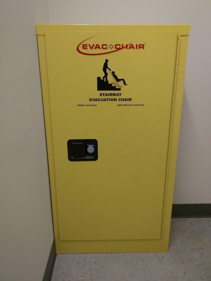 Yellow stairway evacuation chair cabinet against a wall in a school hallway