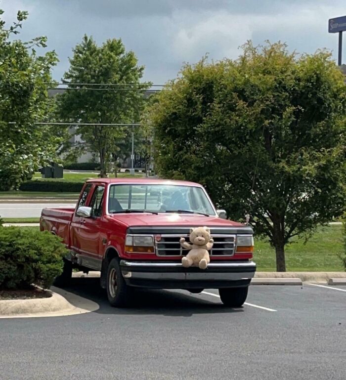Red pickup truck parked with a teddy bear attached to its front grill