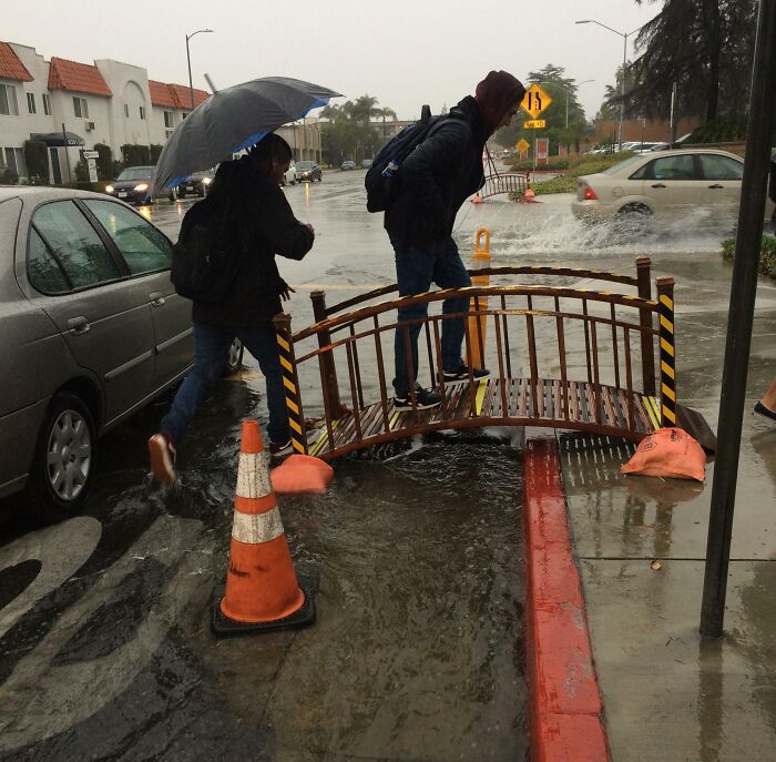Students crossing small bridge over flooded street preventing water on campus