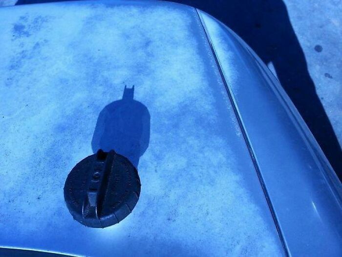 Shadow of a car fuel cap resembles Batman logo on a blue surface