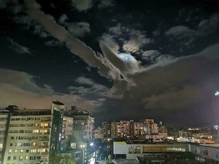 Night cityscape with clouds resembling a flying dolphin and moonlight pareidolia