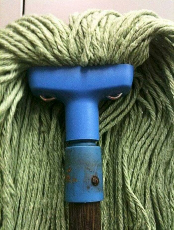 Mop head with strands resembling green hair and face-like features from handle