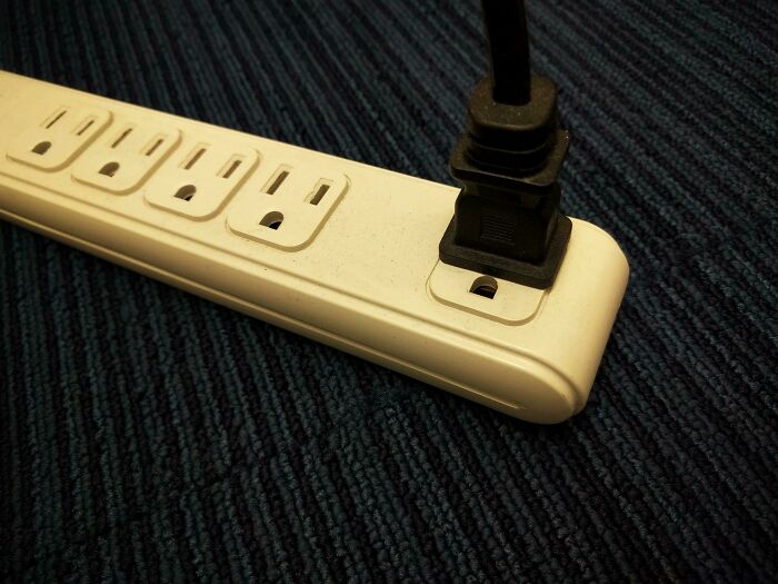Power strip with one plug inserted resembling a sad or surprised face pareidolia