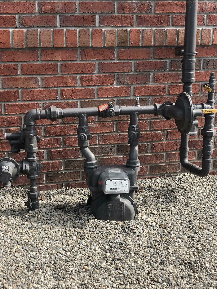 Black gas meter and pipes against red brick wall form a face shape