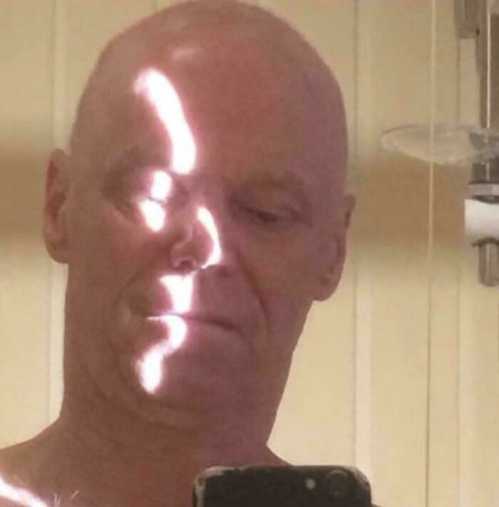 Sunlight shadow on bald man's face creates a bright line resembling facial features