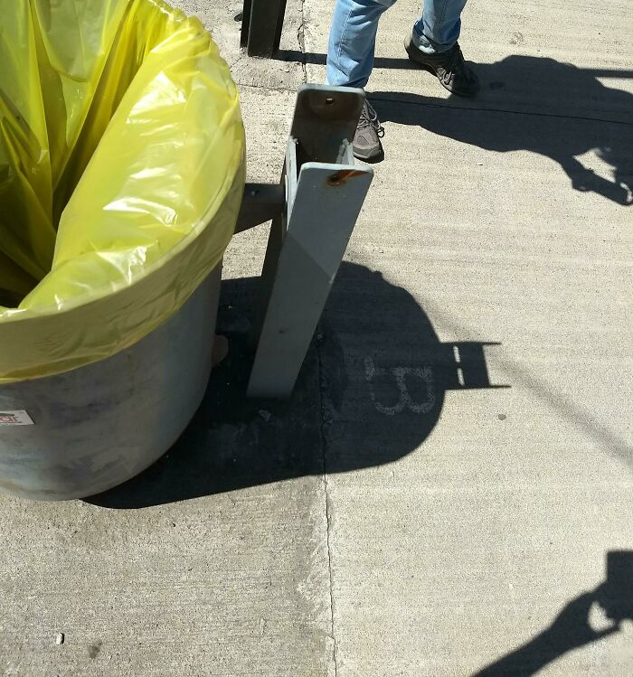 Shadow of trash can holder on sidewalk mimics a face with sunglasses