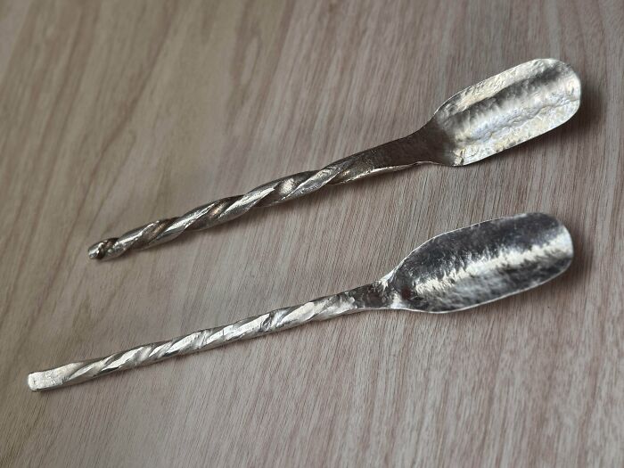 Two handmade metal spoons with twisted handles, a talent-filled project displaying craftsmanship.