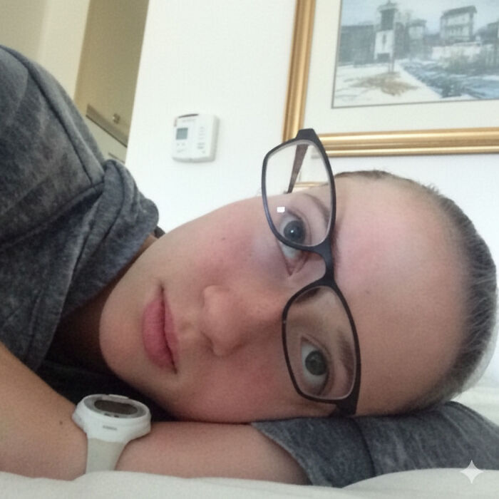 A young woman with glasses and a white watch, lying down and looking up, embodying suspiciously relatable memes.