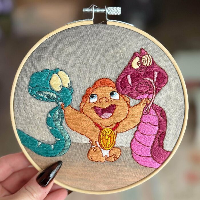 Embroidery projects featuring baby Hercules smiling between two stitched snakes in a hoop