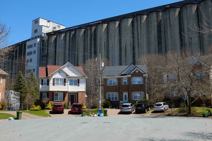 Urban hell with homes overshadowed by large concrete silo walls on sunny day