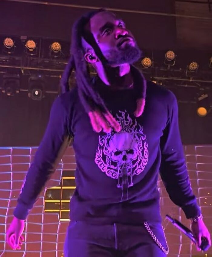 Shaboozey performing on stage, bathed in purple light, wearing a black shirt with a skull design. Bio and career highlights.