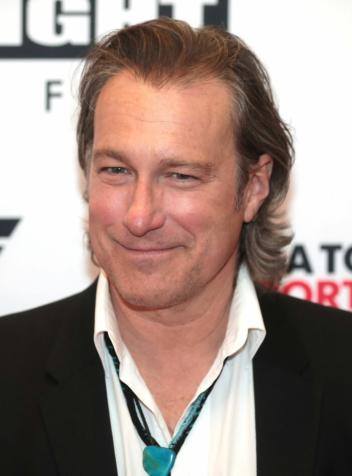 John Corbett, sporting a bolo tie and black jacket, smiles subtly. His career highlights include many recognizable roles.