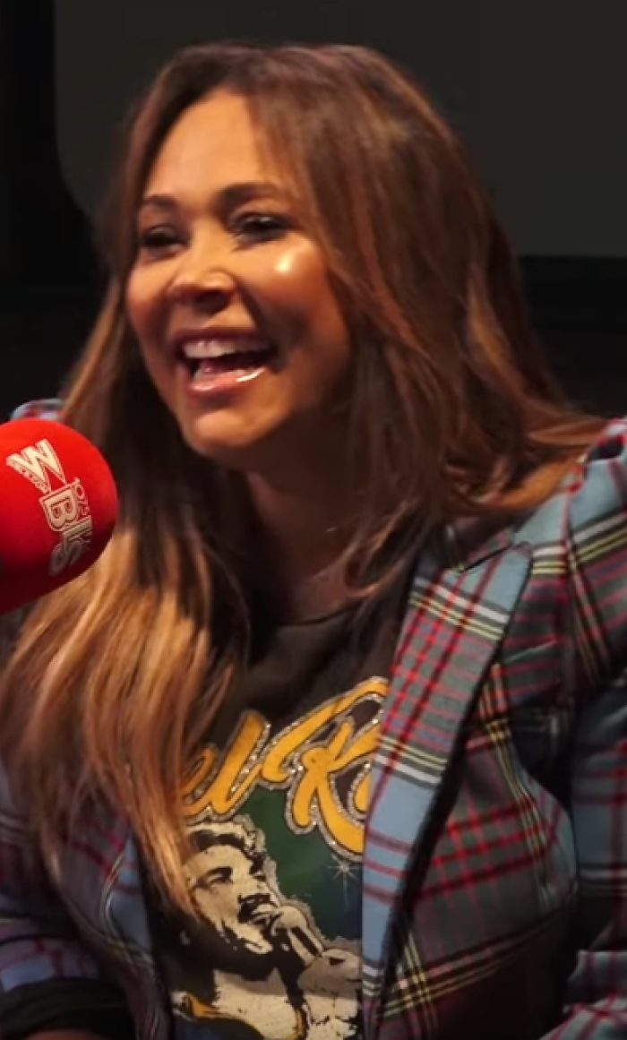 Tamia, laughing joyfully, wearing a plaid jacket and a graphic t-shirt, beside a red microphone. #Tamia #career