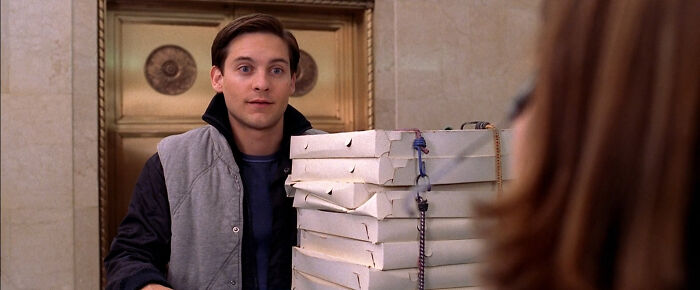 Tobey Maguire as Peter Parker delivers a tall stack of pizza boxes, showcasing hilarious movie details.