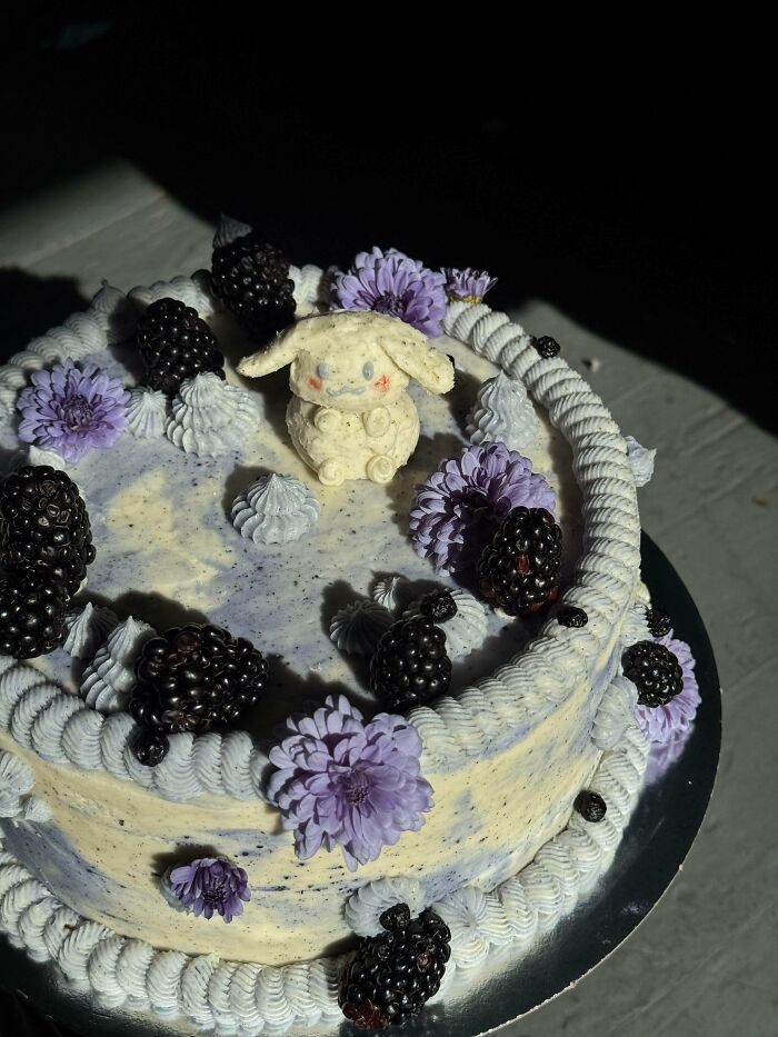 Cake decorated with blackberries, purple flowers, and a fondant animal figure