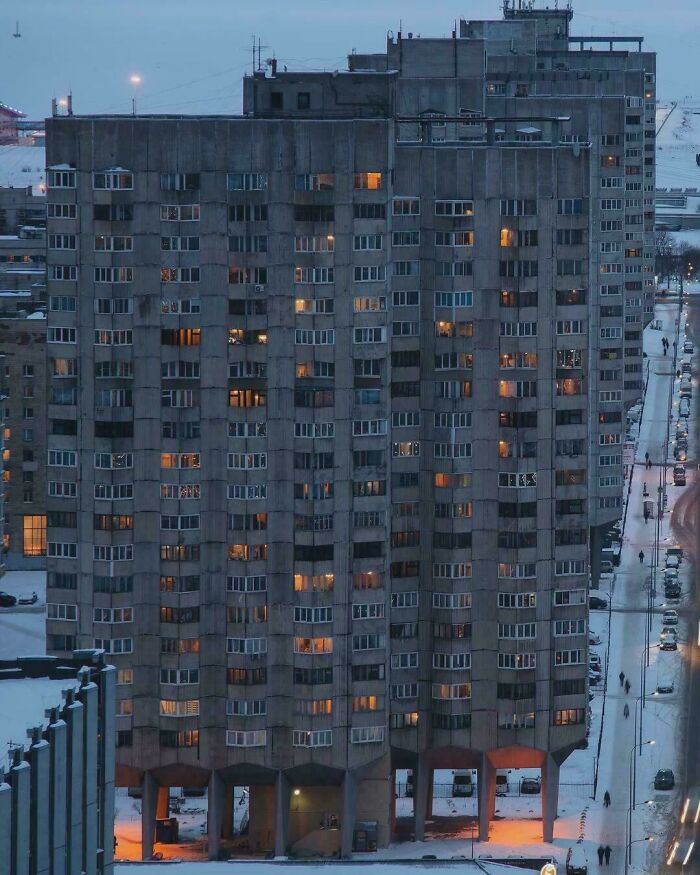 Tall brutalist urban apartment building illuminated at dusk in snowy cityscape
