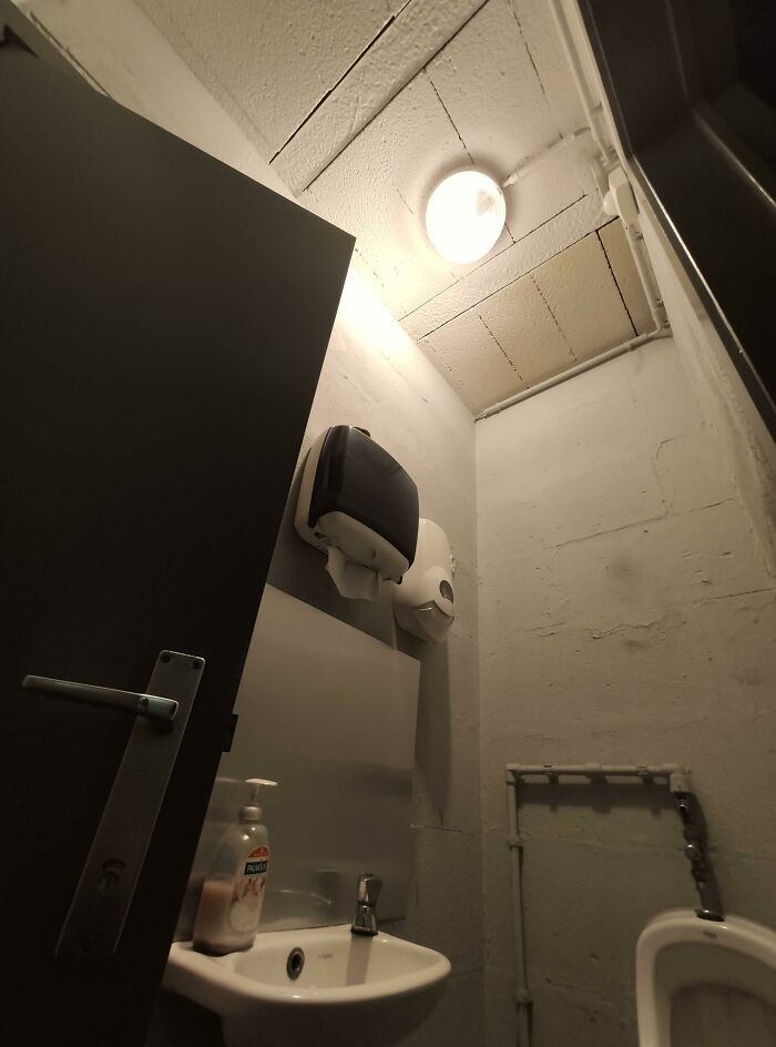 Tiny bathroom with a sink, soap dispenser, and urinal in a cramped space with exposed pipes