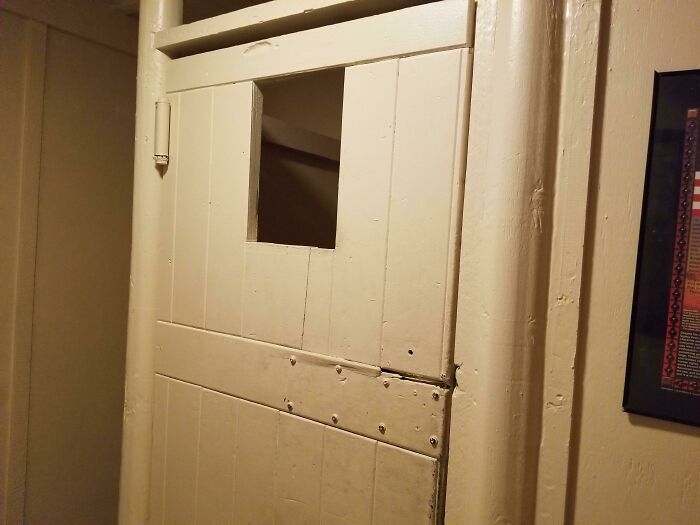Old wooden bathroom door with a small square cut-out window in an unusual design