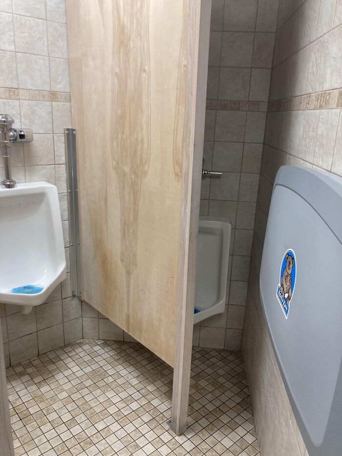 Public restroom urinals awkwardly divided by a partial wooden partition blocking privacy