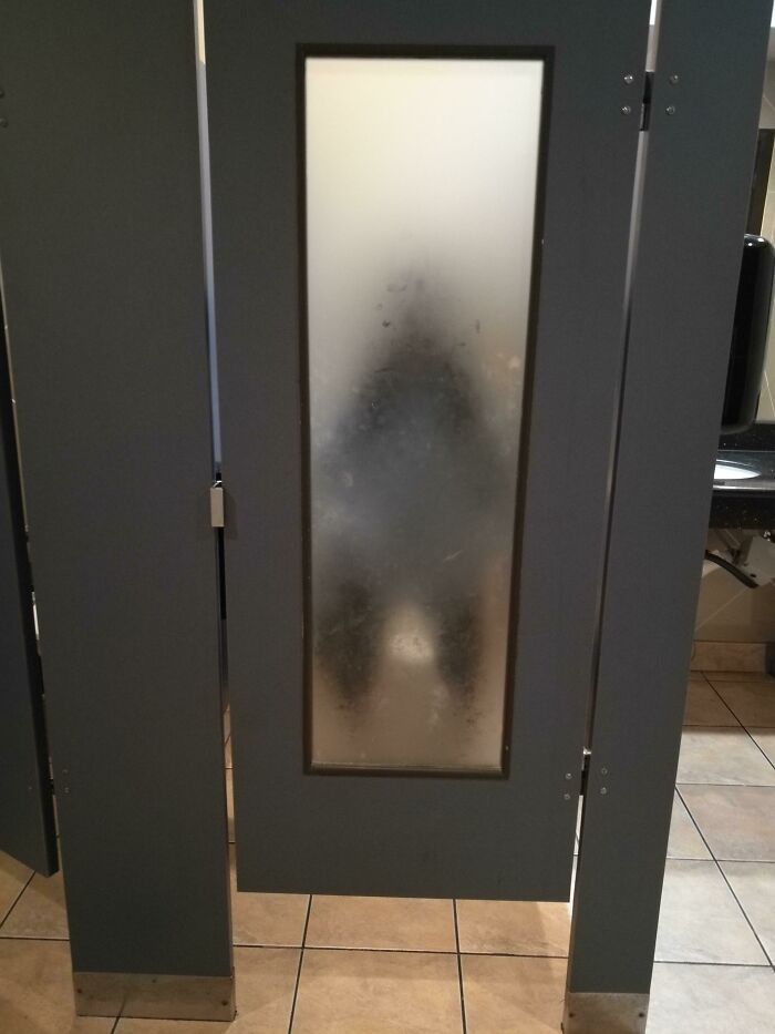 Bathroom stall door with frosted glass panel revealing blurry silhouette inside