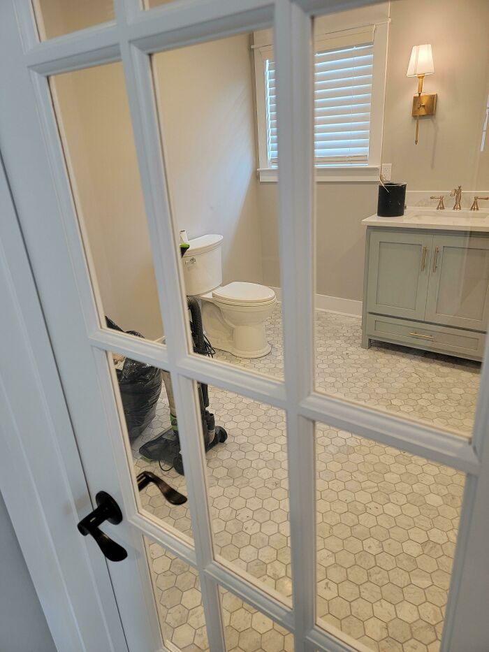 Bathroom with clear glass door exposing toilet and vacuum cleaner inside