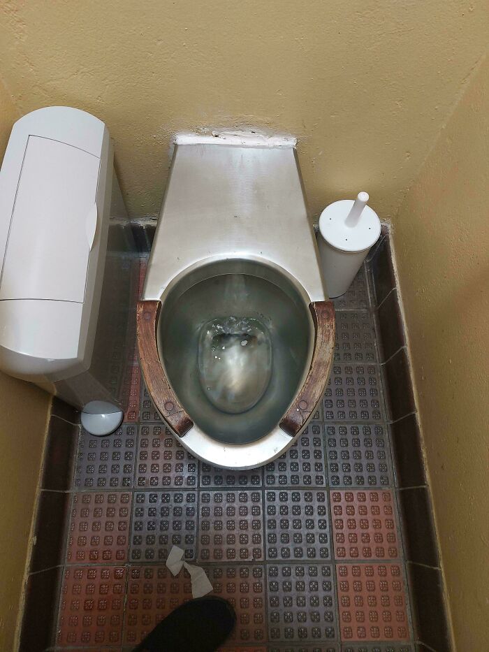 Rusty metal toilet with wooden seat in a cramped bathroom with odd design