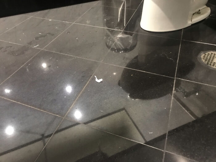 Wet, shiny black tiled bathroom floor near a toilet and drain with reflections