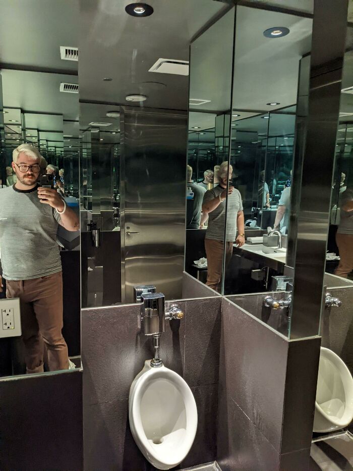 Mirrored bathroom with urinal and man taking selfie reflected multiple times
