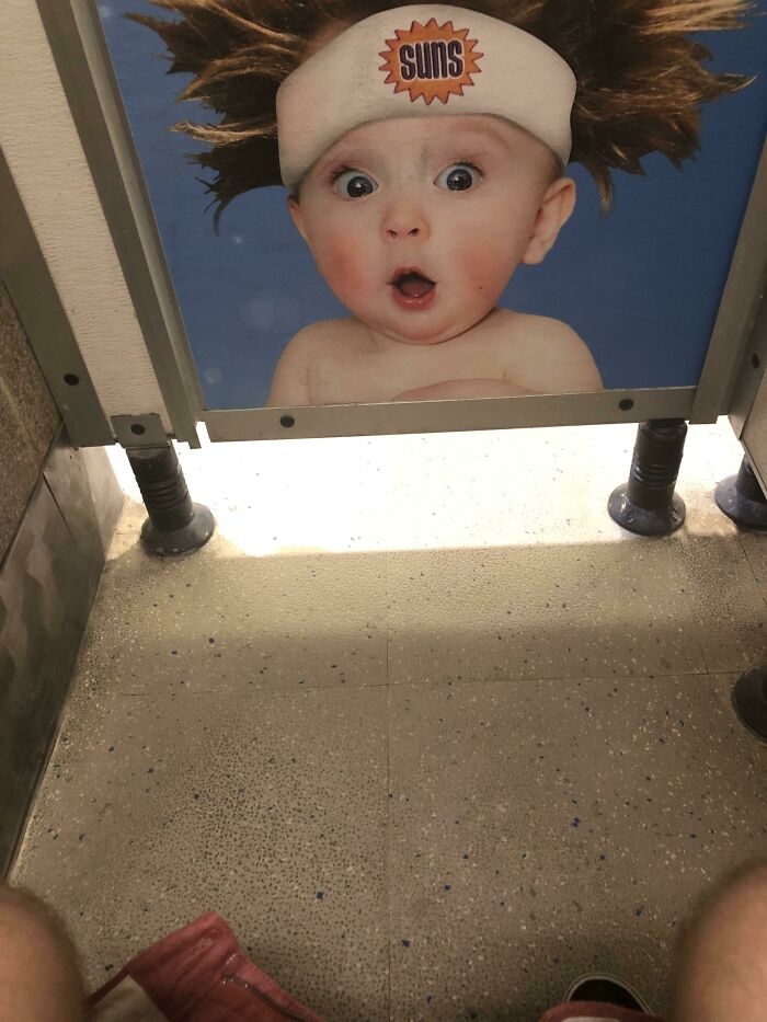 Bathroom stall door with baby photo and Suns headband visible from inside