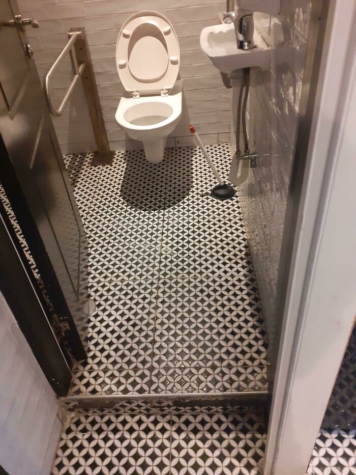 Bathroom with patterned tile floor showing raised step before toilet causing hazard