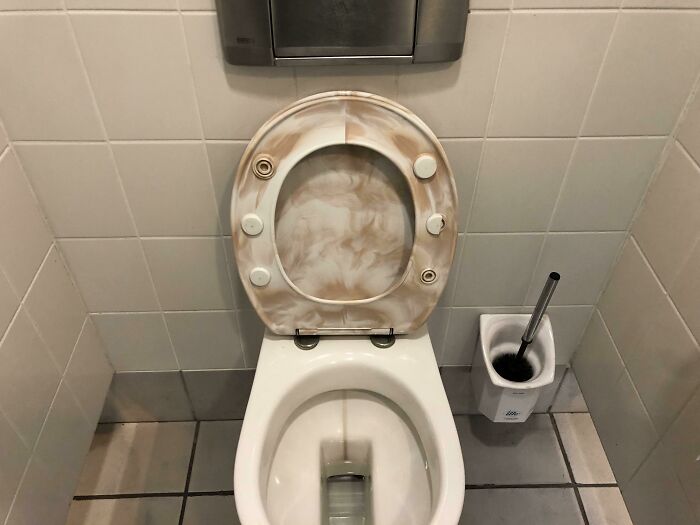 Toilet with worn and stained toilet seat in a tiled bathroom stall