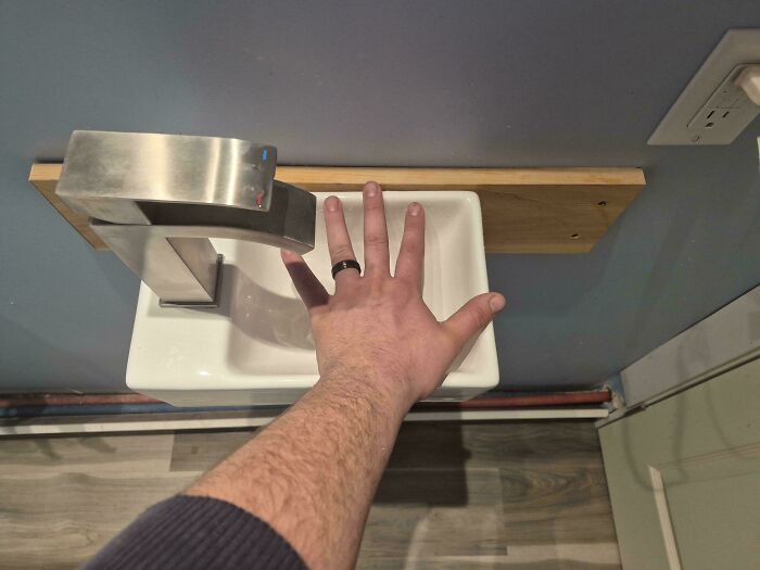 Tiny handwashing sink with hand covering faucet in cramped bathroom space