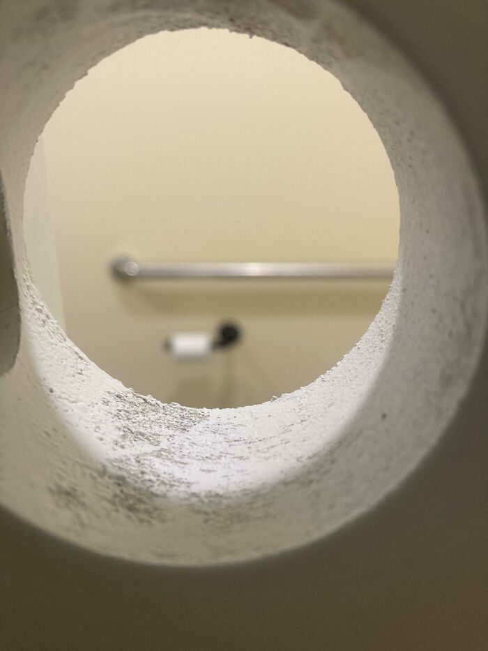View through round hole showing bathroom towel rack and toilet paper