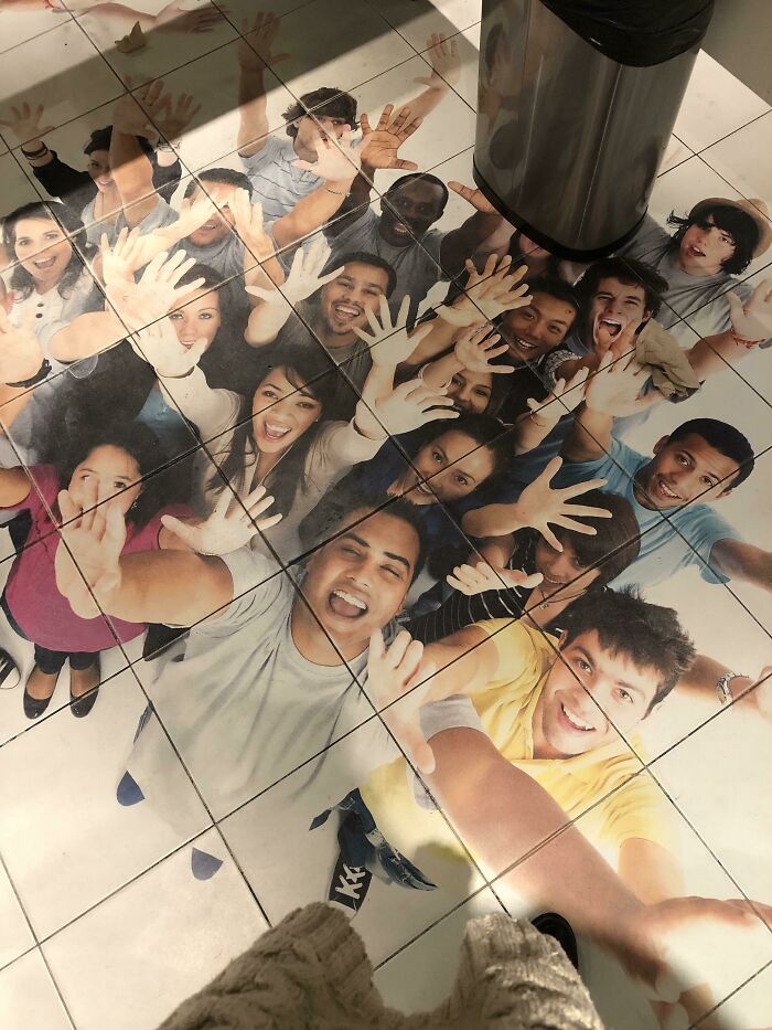 Bathroom floor with tile design of people waving under a trash can