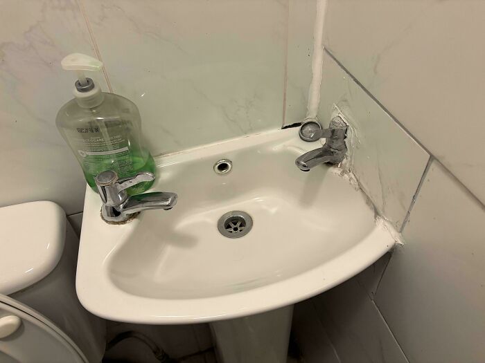 Tiny corner sink in bathroom with awkward faucet placement