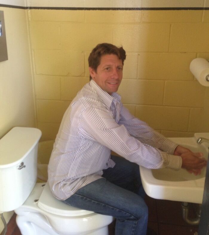 Man washes hands sitting on toilet in strange bathroom design