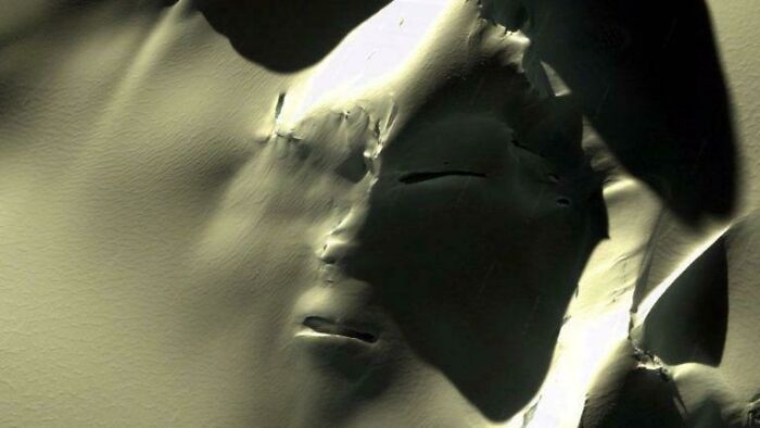 Alien-like face formed by shadows and light on a textured surface, evoking high strangeness.