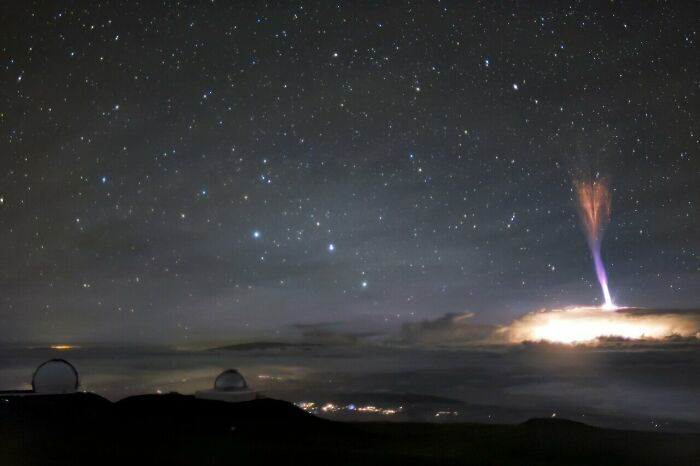 Night sky with stars, two observatories on hills, and a giant red sprite electric discharge above clouds, showing high strangeness.