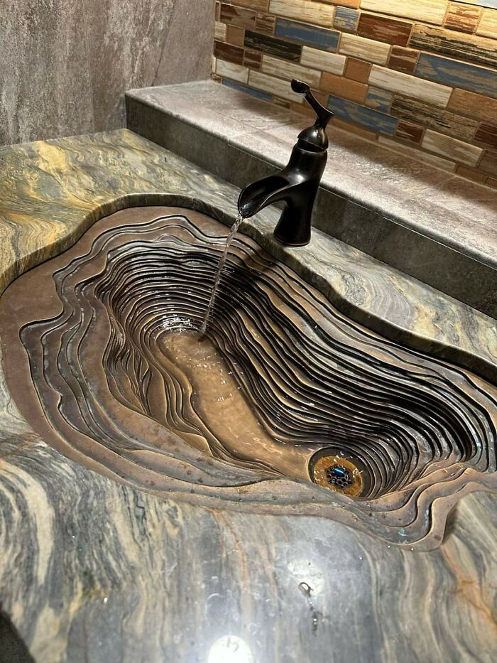 Unique carved layered sink design under running faucet neglecting practical cleaning