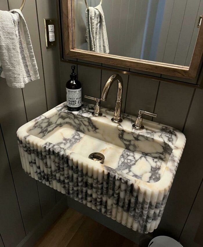 Marble bathroom sink with ridged design and silver faucet under wooden mirror