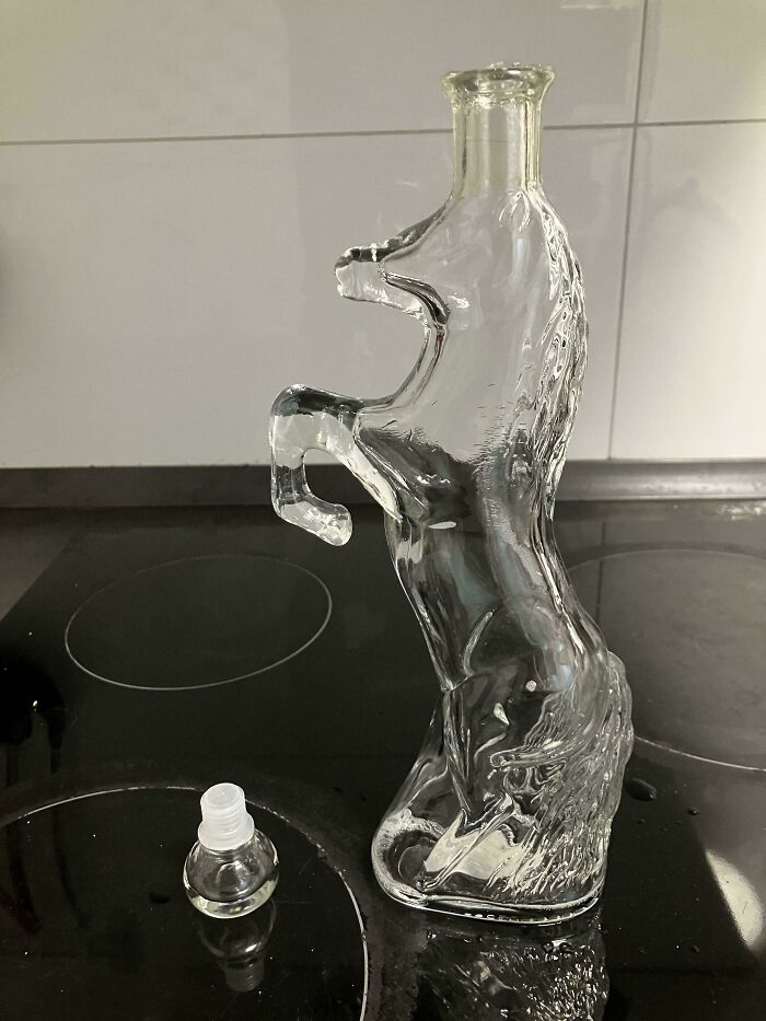 Clear glass bottle shaped like a rearing horse on black countertop