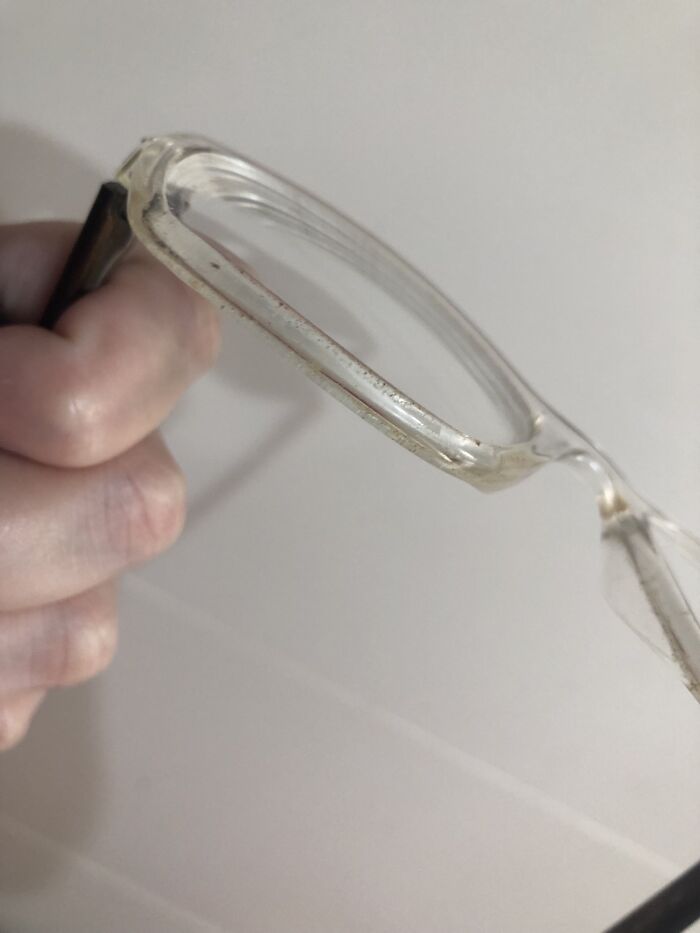 Clear eyeglasses with dirty, dusty frames held in a hand