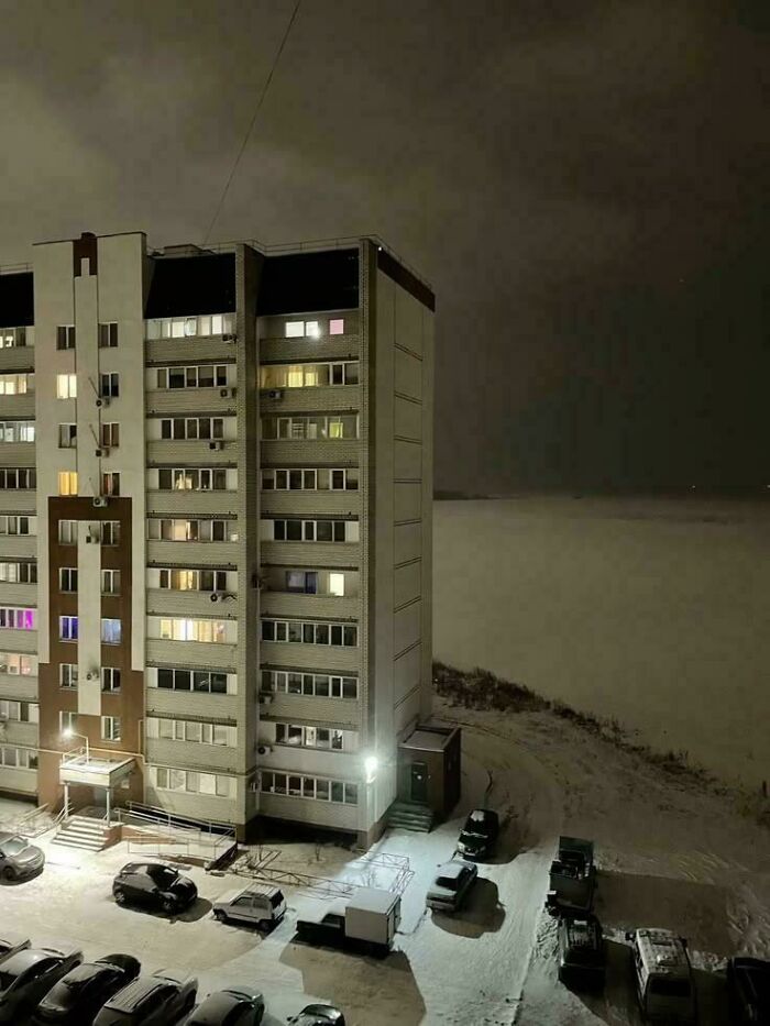 Snow-covered urban apartment building at night with parked cars under street lights