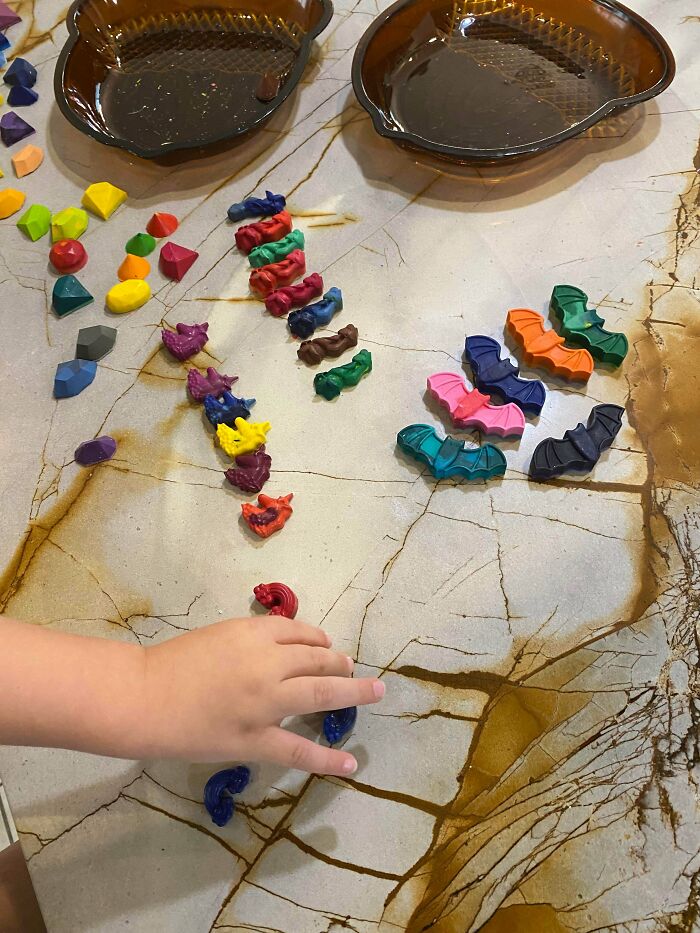 A child's hand near colorful, oddly shaped crayons on a marble table, reflecting consumerism in children's products.